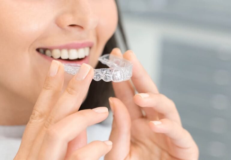 Mujer sonriendo mientras se coloca una férula de ortodoncia invisible tipo invisalign en una clínica dental.